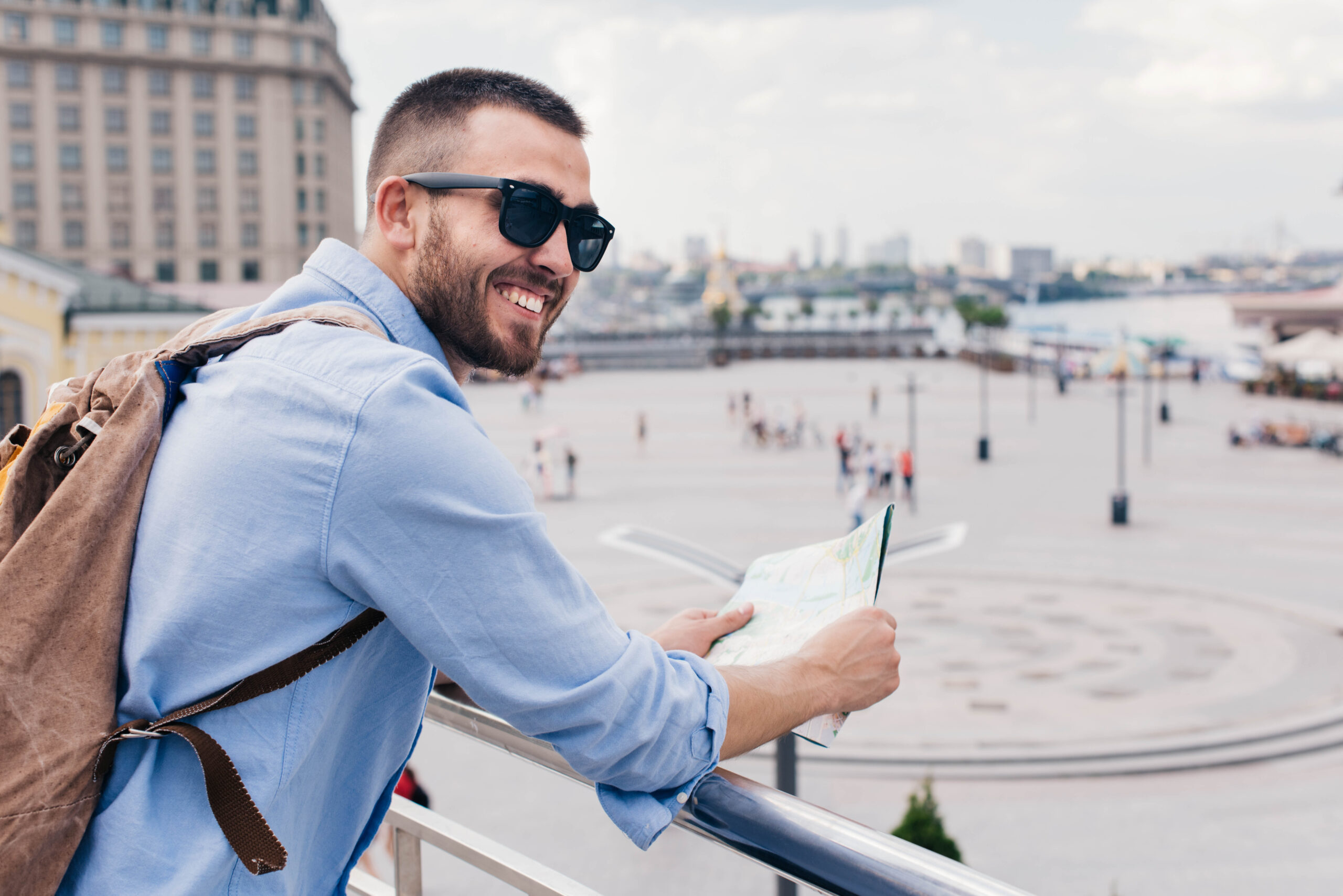 young-bearded-man-carrying-backpack-holding-map-standing-near-railing